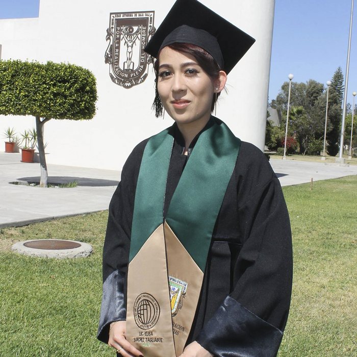 Egresada con estola bordada frente al escudo de la UABC